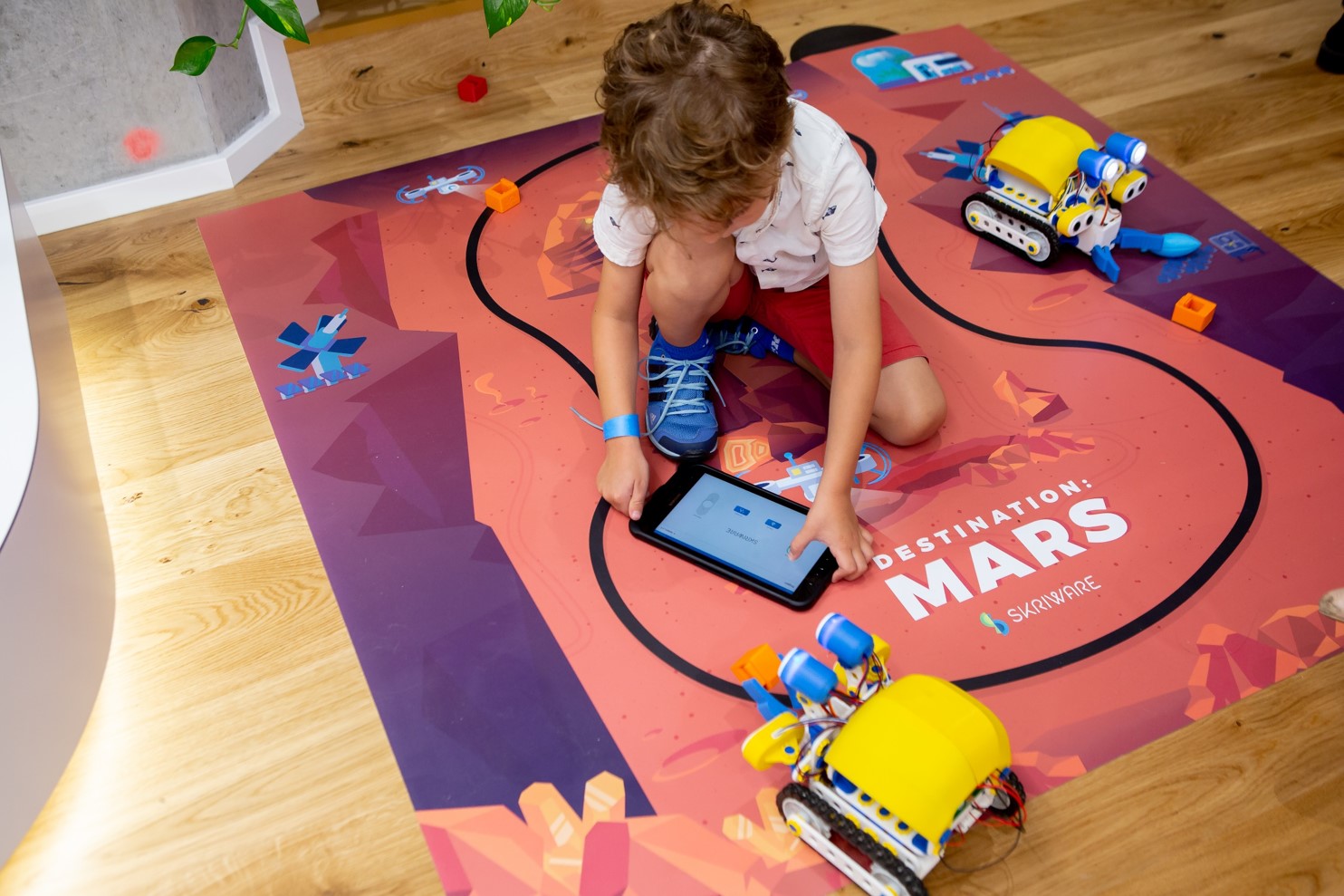 Na planszy z napisem „Destination Mars”, siedzi chłopiec z tabletem w ręku. Po jego lewej i prawej stronie znajdują się roboty.